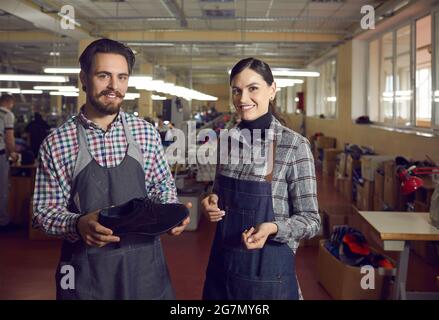 Deux cordonniers divers en uniforme souriant posant pour la caméra avec une chaussure faite à la main Banque D'Images