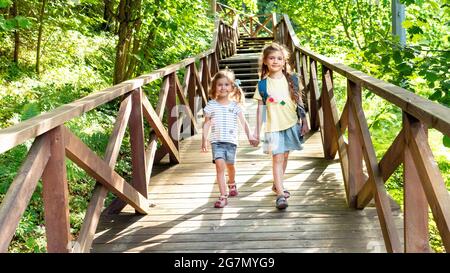 Les enfants qui ont des émotions positives voyagent sur une route de randonnée jusqu'à la réserve. Deux filles souriantes se dirigent vers le camping familial le long d'une route en bois. Visite pour enfants Banque D'Images