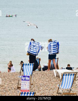 Brighton Royaume-Uni 15 juillet 2021 - ces femmes se rendent à Brighton Beach avec leurs chaises portatives tandis que les visiteurs apprécient un mélange de soleil et de nuages lors d'une journée chaude et brumgy le long de la côte sud. Une vague de chaleur est prévue pour plus tard dans la semaine et le week-end à travers la Grande-Bretagne avec des températures qui devraient atteindre le centigrade élevé de 20s dans certaines parties : crédit Simon Dack / Alamy Live News Banque D'Images