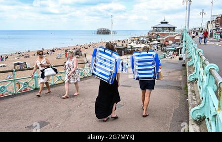 Brighton Royaume-Uni 15 juillet 2021 - ces femmes se rendent à Brighton Beach avec leurs chaises portatives tandis que les visiteurs apprécient un mélange de soleil et de nuages lors d'une journée chaude et brumgy le long de la côte sud. Une vague de chaleur est prévue pour plus tard dans la semaine et le week-end à travers la Grande-Bretagne avec des températures qui devraient atteindre le centigrade élevé de 20s dans certaines parties : crédit Simon Dack / Alamy Live News Banque D'Images