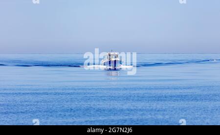 Bateau à moteur naviguant sur fond de mer Egée et ondulé, sentier sur une eau calme. Grèce, Cyclades. Surface d'eau plate, ciel clair. Vacances d'été concep Banque D'Images