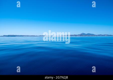 Grèce, Cyclades. Mer Egée, surface d'eau plate, ciel clair. Terre rocheuse de l'île grecque et arrière-plan de nuances bleues. Voile dans un calme bleu foncé ocea Banque D'Images