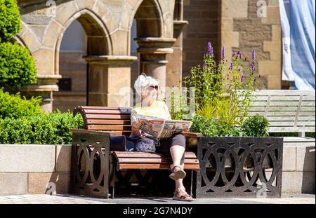 Dundee, Tayside, Écosse, Royaume-Uni. 15 juillet 2021. Météo au Royaume-Uni : soleil chaud dans le nord-est de l'Écosse avec des températures atteignant 20°C. Une femme âgée prend la journée pour profiter du temps de l'été tout en étant assise sur un siège lisant le journal télégraphique du soir dans le centre-ville de Dundee. Crédit : Dundee Photographics/Alamy Live News Banque D'Images