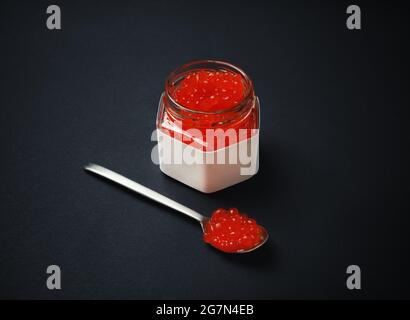Caviar rouge frais, pot en verre et cuillère sur fond noir. Banque D'Images