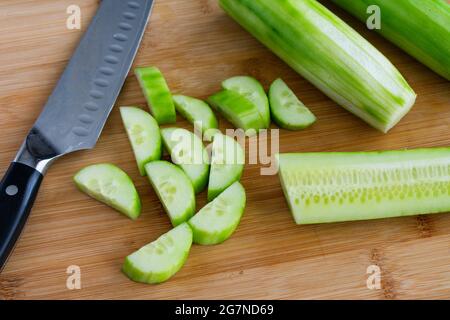 Trancher un concombre anglais de moitié : trancher un concombre de huche épluché et coupé de moitié sur une planche à découper en bambou Banque D'Images