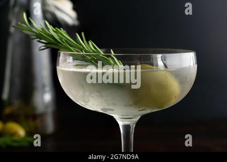 Martini sale à l'huile de romarin fumé : martini de gin sale servi dans un verre de coupé et garni d'une branche de romarin dans une olive verte Banque D'Images