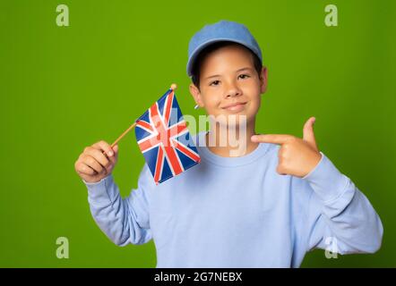 Mignon garçon dans des vêtements décontractés posant avec drapeau britannique isolé sur fond vert. Banque D'Images