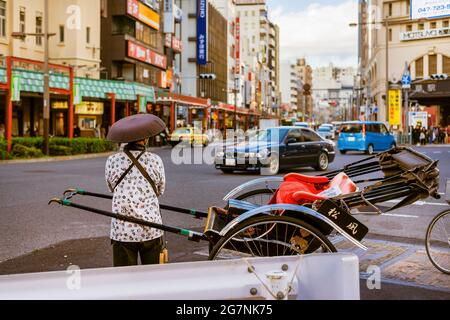 Japon entre tradition et modernité. Un coureur en pousse-pousse regarde les voitures modernes du carrefour d'Asakusa à Tokyo Banque D'Images