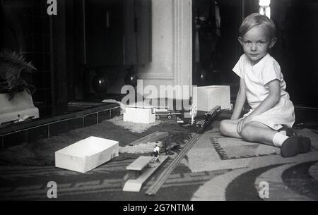 Années 1950, jeune garçon historique dans un salon assis sur un tapis devant une cheminée avec son train, Angleterre, Royaume-Uni. Banque D'Images