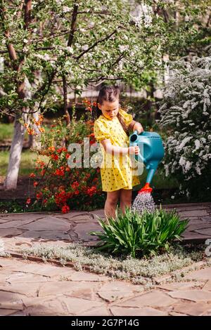 un petit jardinier est arroser des fleurs d'un arrosoir, une fille est jardinage dans l'arrière-cour dans un jardin de printemps en fleur Banque D'Images