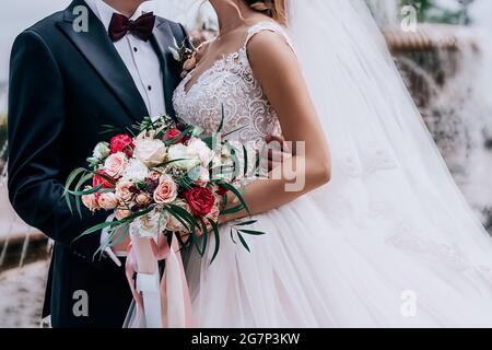 Beau couple avec un bouquet de mariage étonnant de roses rouges, blanches, beiges Banque D'Images