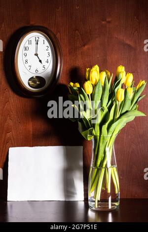 horloge murale, feuille de papier vierge et tulipes dans un vase sur fond de bois brun foncé Banque D'Images