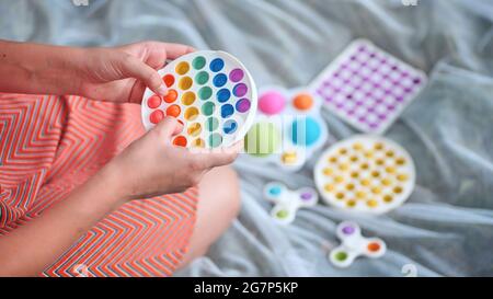 Une jeune fille joue avec des jouets multicouleurs anti-stress popit et des fossettes simples dans le parc lors d'une journée d'été. Banque D'Images