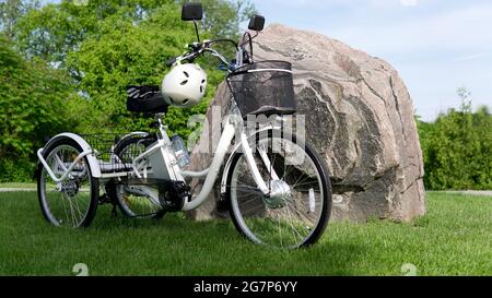 Vélo électrique sur l'herbe verte avec fond de pierre le jour d'été ensoleillé. Prise de vue latérale. Beaucoup d'éclairage naturel. La vue du moteur électrique, Banque D'Images