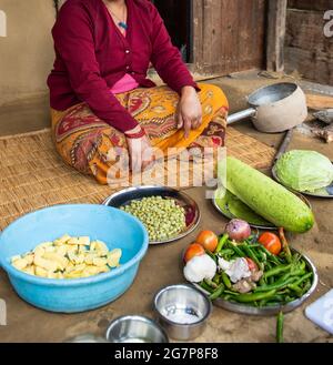 Une femme habillée de vêtements colorés, assise à l'extérieur de sa maison pour préparer des légumes au Népal. Banque D'Images
