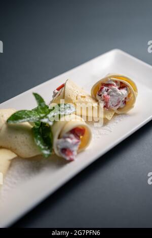 petits rouleaux de crêpes avec fromage cottage à la crème et fraise sur fond noir Banque D'Images