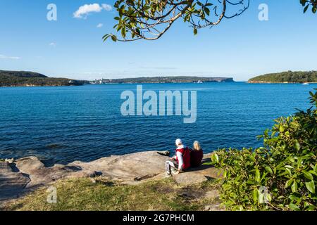 Couple assis et reposant sur une journée ensoleillée à Balmoral Beach, Sydney, Australie, pendant le confinement pandémique. Vue sur le port de Sydney Banque D'Images