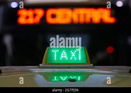 Panneau de cabine de taxi allumé sur le dessus du véhicule la nuit. Feux de circulation de la ville avec couleur néon en arrière-plan. Banque D'Images
