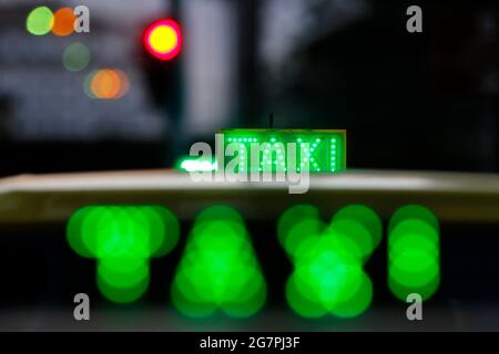 Panneau de cabine de taxi allumé sur le dessus du véhicule la nuit. Feux de circulation de la ville avec couleur néon en arrière-plan. Banque D'Images