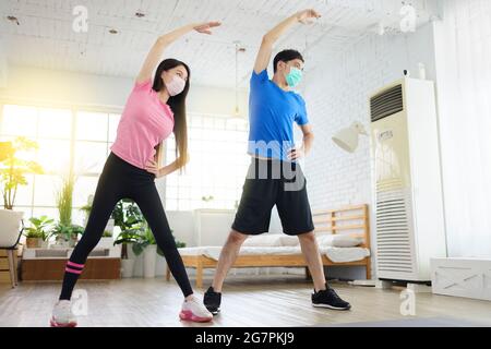 Les jeunes couples portent des masques médicaux et font de l'exercice à la maison. Banque D'Images