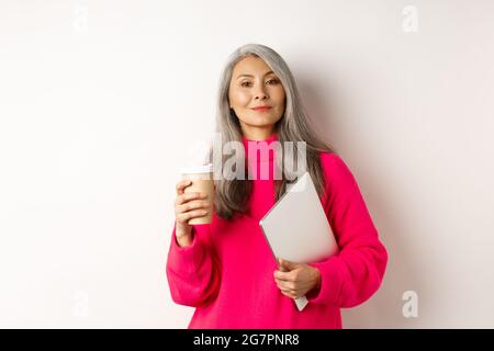 Femme d'affaires asiatique élégante et sénior, se tenant autour d'un ordinateur portable, se tenant debout sur un fond blanc et en toute confiance Banque D'Images