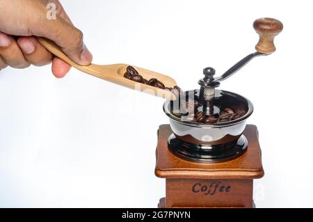 un homme verse des grains de café à la main, de la cuillère en bois au moulin à café, sur fond blanc Banque D'Images