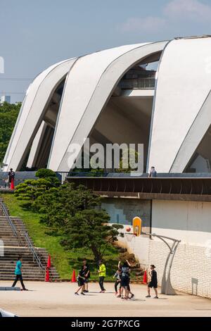 Le stade d'athlétisme conçu par Masachika Murata en arrière-plan, les jeunes jouent au basket-ball dans le parc olympique de Komazawa, à Tokyo, le 10 juin 2021. Le parc a été construit pour les Jeux Olympiques de 1064 et reste un lieu de loisirs populaire. Robert Gilhooly photo Banque D'Images