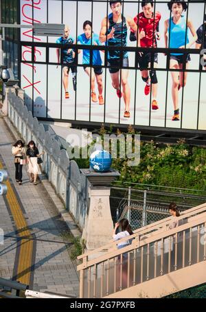 Les piétons passent par le pont olympique près du parc Yoyogi, Tokyo, le 21 juin 2021. Alors que le pont faisait partie d'un nouveau réseau routier construit avant les Jeux Olympiques de 1964, les globes au sommet des piliers et des reliefs de pierre sur le thème des Jeux Olympiques ont été ajoutés plus de 25 ans plus tard. Robert Gilhooly photo Banque D'Images