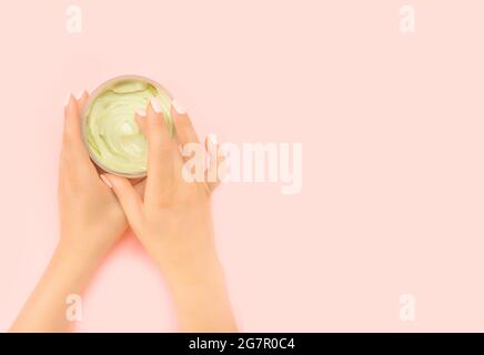 Femme tenant un pot crème hydratante, faisant soin de beauté à la maison. Pot crème anti-âge est tenu dans les mains de la femme avec une belle manucure. Naturel Banque D'Images