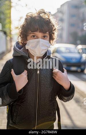 Écolier avec sac à dos de retour à l'école avec masque facial. Jeune de neuf ans marchant dans la rue dans le coronavirus nouvelle norme. Banque D'Images