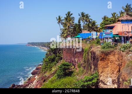 Palmiers et restaurants et cabanes au sommet d'une falaise surplombant la mer d'Arabie avec un ciel bleu à Varkala, Kerala, Inde Banque D'Images