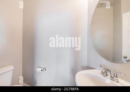 Mur blanc de la salle de bains avec grand miroir ovale au-dessus du lavabo Banque D'Images