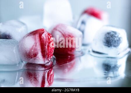 Gros plan des framboises et des bleuets congelés dans des glaçons; fonte des glaçons; arôme d'eau saine; vie libre créative; photographie alimentaire; baies Banque D'Images