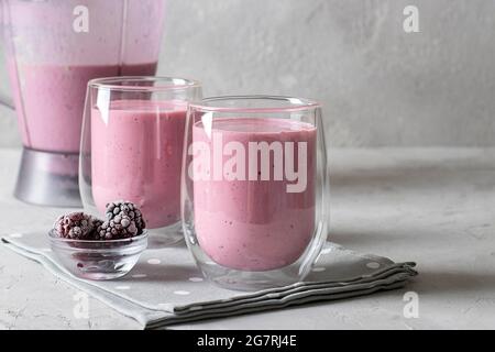 Smoothies faits maison aux mûres glacées dans deux verres transparents et bol mélangeur sur fond gris clair. Copier l'espace Banque D'Images