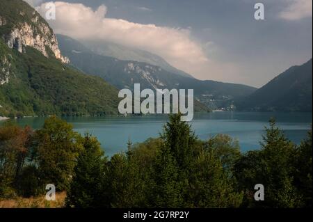 La surface tranquille du « plus beau lac d'Italie », le Lago di Molveno dans le Trentin-Haut-Adige, passe du vert profond au bleu pâle à mesure que les nuages s'amassent au-dessus des sommets des Dolomites de Brenta, les forêts denses vêtues de leurs pentes et les arbres à feuilles persistantes qui poussent le long du front de mer. Le lac a été décrit en 1890 par le poète et romancier italien Antonio Fogazzaro comme « la perle précieuse dans un cercueil encore plus précieux ». Les eaux alpines, jusqu'à 124 m (406 pi) de profondeur, cachent une forêt pétrifiée d'abord submergée il y a environ 3,000 ans, au début de l'âge du fer. Banque D'Images