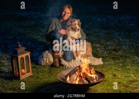 Le chien est assis près du feu de camp avec son propriétaire. La femme regarde avec amour le Berger allemand. Vacances en hiver, feu de bougie dans lanterne Banque D'Images