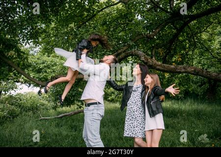 De jeunes parents heureux jouant avec de jolies petites filles dans un jardin verdoyant. Les familles caucasiennes passent des week-ends en s'amusant à l'air frais. Concept de relation et de parentalité. Banque D'Images