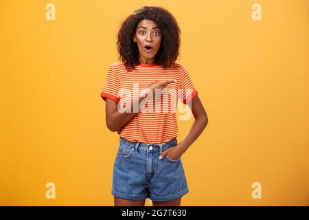 Photo en studio d'un modèle féminin élégant en short denim et un t-shirt qui se déva a impressionné de pointer du bon côté tout en posant la question intéressé pendant Banque D'Images