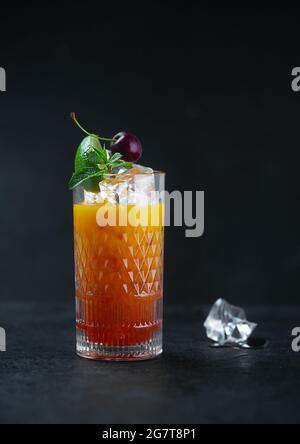 Jus d'orange avec glace à la menthe et à la cerise dans un verre sur fond sombre. Touche Bas Banque D'Images