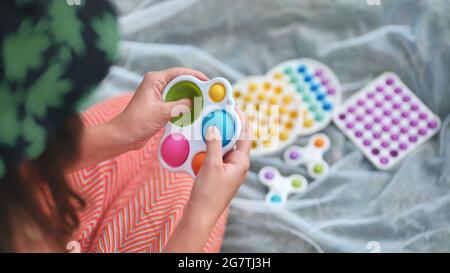 Une jeune fille joue avec des jouets multicouleurs anti-stress popit et des fossettes simples dans le parc lors d'une journée d'été. Banque D'Images
