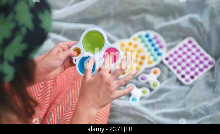Une jeune fille joue avec des jouets multicouleurs anti-stress popit et des fossettes simples dans le parc lors d'une journée d'été. Banque D'Images