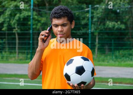 Homme brésilien tenant le ballon de football et utilisant un smartphone sur les terrains de sport Banque D'Images