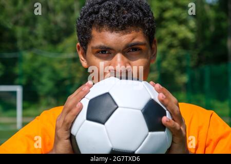 L'homme brésilien tient le ballon de football de près tout en se tenant sur le terrain de sport Banque D'Images