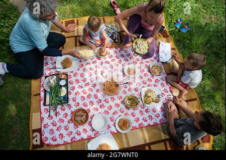 Vue de dessus d'une famille ayant un pique-nique dans la nature assis sur une couverture pleine de nourriture et d'encas délicieux. Banque D'Images