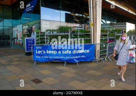 Talaplow, Buckinghamshire, Royaume-Uni. 16 juillet 2021. Les clients marchent devant une bannière "let's Keep a safe distance" à l'extérieur du supermarché Tesco de Talalow. La majorité des grands supermarchés en Angleterre demandera aux clients de continuer à porter un masque dans leurs magasins à partir du lundi 19 juillet 2021, malgré la levée des restrictions de verrouillage de Covid-19. La politique sera uniquement consultative pour les clients et ne sera pas juridiquement applicable. Crédit : Maureen McLean/Alay Banque D'Images