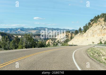 Lonely road between mountain ridges with some trees on each side of the road that turns to the right, somewhere in Utah, United States Stock Photo