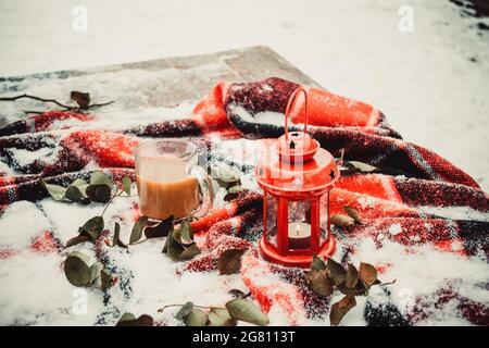 Bougie rouge festive dans une lanterne et une tasse de café sur un tapis enneigé Banque D'Images