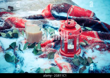 Bougie rouge festive dans une lanterne et une tasse de café sur un tapis enneigé Banque D'Images