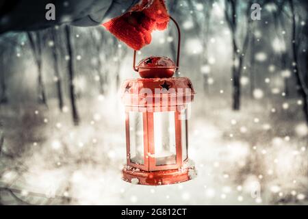 Tenue d'une lanterne de bougie rouge dans la forêt d'hiver. Banque D'Images