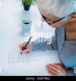 Femme senior résolvant le puzzle sudoku Banque D'Images